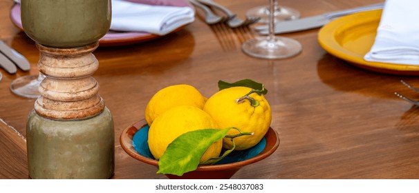 Mediterranean-inspired dining table with a ceramic bowl of vibrant yellow lemons and green leaves, complemented by plates, napkins and cutlery, perfect for culinary, lifestyle or hospitality content. - Powered by Shutterstock