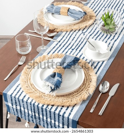 Mediterranean-Inspired Summer Table Setting Featuring Crisp White Porcelain on Natural Woven Raffia Placemats, with Bold Blue Striped Linen Table Runner and Matching Napkins,Clear Glass Stemware.