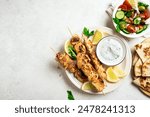 Mediterranenan food: chicken skewers, flatbread and vegetable salad. Roasted souvlaki, greek salad, tzatziki yogurt sauce and pita bread on white background, copy space.