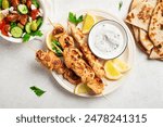 Mediterranenan style healthy lunch: chicken skewers, flatbread and vegetable salad. Fried souvlaki, greek salad, tzatziki yogurt sauce and pita bread on white table.