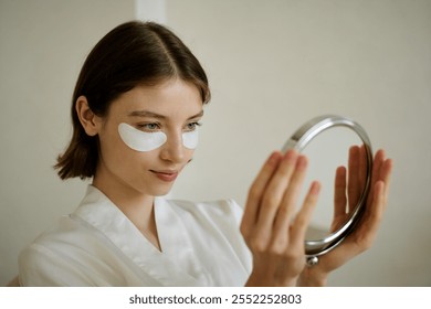 Medium close up of attractive woman with hydrogel eye patches admiring herself in mirror - Powered by Shutterstock