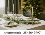 Medium close up of festive table decorated with polished champagne glasses and white plates, center of table decorated with amazing pine garland