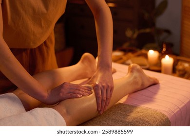 Medium close up of unrecognizable professional spa worker massaging calf of female client