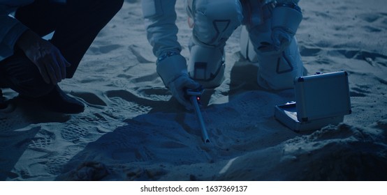 Medium close-up of an astronaut and a scientist testing sample collector tool
