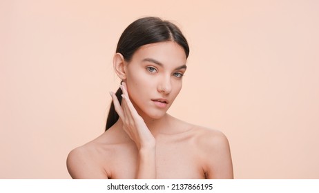 Medium close-up beauty portrait of Young slim woman who gently touches her jawline and looks at the camera | Beauty and skin care concept