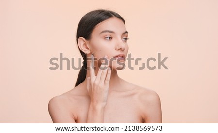 Medium close-up beauty portrait of Young slim woman who gently touches and strokes her jawline and look at the camera. Beauty and skin care concept