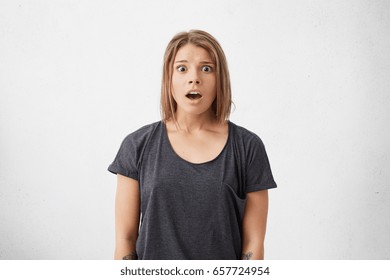 Medium Close-up Of Frightened Excited Woman With Trendy Hairstyle Looking With Big Eyes And Opened Mouth Into Camera Being Surprised To See Someone. Cute Lady With Shocked Expression Posing In Studio