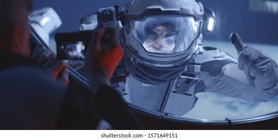 Medium Close-up Of A Male Astronaut Filming His Spacewalking Crewmate From Inside A Spacecraft