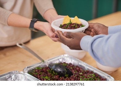 Medium close-up shot of unrecognizable volunteer giving plate with meal to beneficiaries in charity canteen - Shutterstock ID 2138297761
