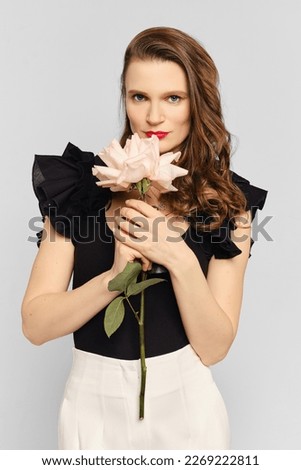 Medium closeup studio portrait of cute woman sniffs beautiful flower