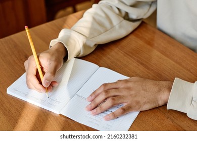 Medium close-up of unrecognizable young man sitting at desk at school writing something in notebook - Shutterstock ID 2160232381