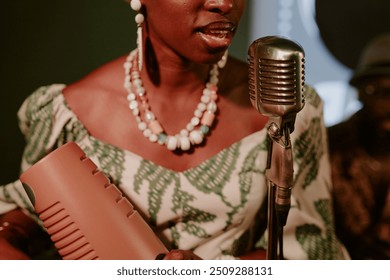 Medium closeup of young African American woman holding guiro in hands singing jazz song in microphone - Powered by Shutterstock