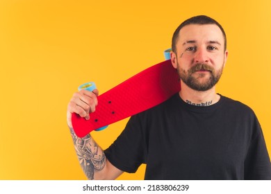 Medium Closeup Of Young Caucasian Man With A Tattoo On His Face Holding Red Skateboard On His Shoulder Yellow Background Studio Shot Copy Space . High Quality Photo