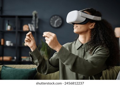 Medium closeup of young woman wearing VR headset sitting on sofa in living room playing video game or working - Powered by Shutterstock