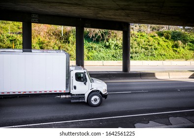 Medium duty rig compact size white industrial semi truck for local deliveries transporting commercial cargo for timely delivery in dry van box trailer running on the divided wide highway road
