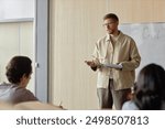 Medium full shot of adult male professor teaching students giving lecture at university hall, copy space