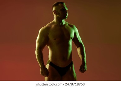 Medium full shot of confident athletic man shirtless showing upper body muscles with hard chest and arm muscles on red background. Studio image of sportsman with contour green and neutral light - Powered by Shutterstock