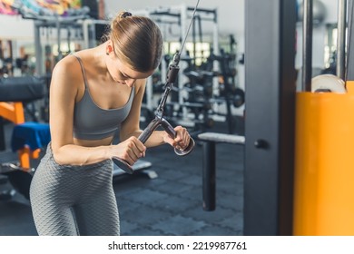 Medium Indoor Shot Of Strong Determined Caucasian Skinny Girl In Her 20s Wearing Stylish Gray Sportswear Exercising At Gym, Using Weight Lifting Machine. High Quality Photo