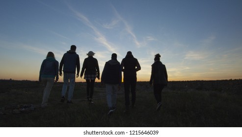 Medium Long Shot From Behind Of A Group Of Friends Walking Together Into The Setting Sun