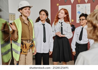 Medium long shot of female engineer wearing safety helmet and vest demonstrating solar panel to group of teen students during career day class - Powered by Shutterstock