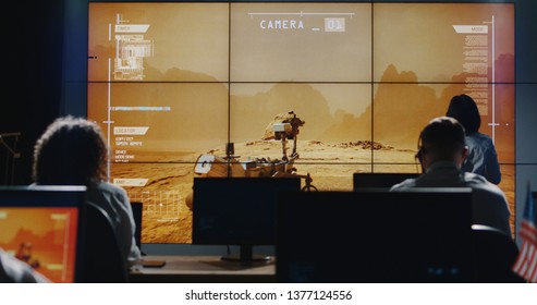 Medium long shot of technicians walking around in control room while Mars Rover moving on digital screen - Shutterstock ID 1377124556