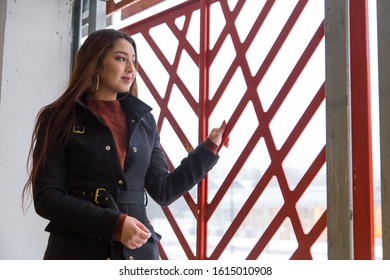 Medium Low Angle Three Quarter Profile View Of Pretty Brunette Woman With Waist Length Hair Wearing Black Coat Looking Out Of The Window Of An Indoor Parking Building