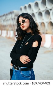 Medium portrait shot of fashionista girl in black sweater and sunglasses standing in sunlight.