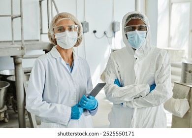 Medium portrait shot of female process technician with digital tablet posing with African American male coworker in coveralls on shop floor at pharmaceutical manufacturing plant - Powered by Shutterstock