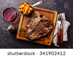 Medium rare Grilled T-Bone Steak with potato wedges and wine on serving board block on dark background