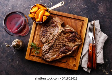 Medium Rare Grilled T-Bone Steak With Potato Wedges And Wine On Serving Board Block On Dark Background