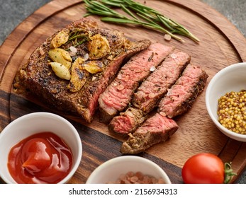 Medium rare Ribeye steak or beef steak on the wooden tray with garlic, ketchup, mustard. Rib eye steak