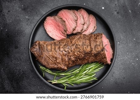 Medium rare roast beef cooked whole and sliced with rosemary. Juicy roasted beef tenderloin served in cast iron pan with copy space