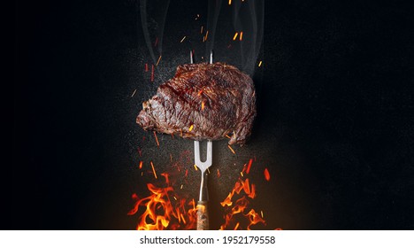 medium rare steak on an iron fork on a dark background. from below, fire and sparks. meat and fire.