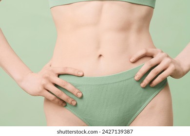 Medium section studio shot of unrecognizable young woman with defined abs wearing mint green ribbed underwear posing for camera