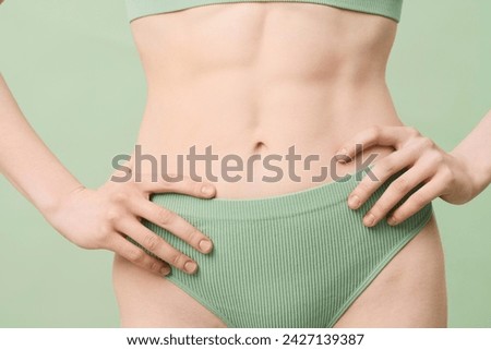 Medium section studio shot of unrecognizable young woman with defined abs wearing mint green ribbed underwear posing for camera