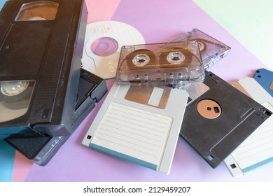 Medium short shot, background depicting elements of the 1990s.Coloured cardboard creating triangular shapes and electronic storage devices, floppy disks, VHS tapes, cassettes and CD.