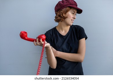 Medium Short Shot Of Young Latin American Woman (22) With Cap And Red Hair, Not Interested In Conversation And Puts Away The Handset Of Her Retro Handset In A Disinterested Way. 