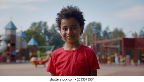 Medium shot of african active little boy on playground looking at camera. Portrait of adorable afro-american preschool child smiling at camera outdoors - Shutterstock ID 2033573534