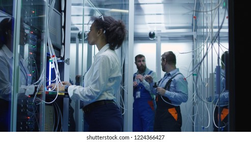 Medium shot of African American women working with cables in a data center server room with rows of server racks against other technicians. - Powered by Shutterstock