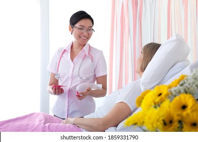 A Medium Shot Of An Asian Nurse Smiling And Talking To A Patient In A Hospital Room.