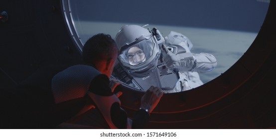 Medium shot of an astronaut talking with his spacewalking crewmate by the spacecraft window - Powered by Shutterstock