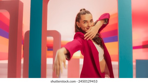 Medium Shot of an Attractive Woman in a Fashionable Outfit Moving her Hands Gracefully While Dancing and Looking at Camera. Female Dancer Performing Choreography in a Spacious Colorful Studio. - Powered by Shutterstock