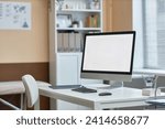 Medium shot of computer monitor with white copy space screen and stationery on table in doctors consulting room