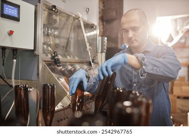 Medium shot of concentrated male production operator in protective gloves carefully sterilizing glass bottles at craft cider or beer factory, copy space - Powered by Shutterstock