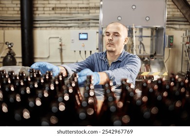 Medium shot of concentrated male production operator grabbing glass bottles from stack - Powered by Shutterstock