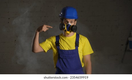 Medium shot of a construction worker standing in the room filled with smoke, happy to wear a respirator and pointing at it. - Powered by Shutterstock