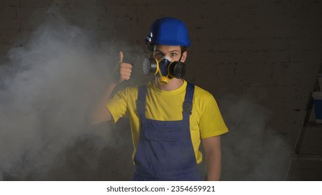 Medium shot of a construction worker standing in the room filled with smoke, happy to wear a respirator and giving a thumbs up. - Powered by Shutterstock