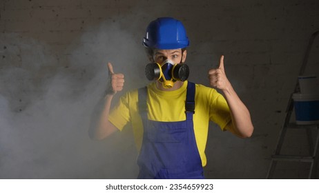 Medium shot of a construction worker standing in the room filled with smoke, happy to wear a respirator and giving a thumbs up. - Powered by Shutterstock