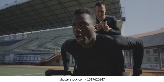 Medium shot of a disabled athlete rolling with wheelchair while being encouraged by his trainer - Powered by Shutterstock