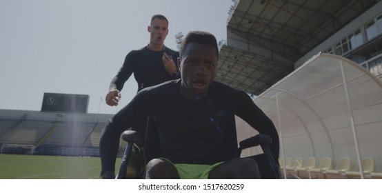 Medium shot of a disabled athlete rolling with wheelchair while being encouraged by his trainer - Powered by Shutterstock